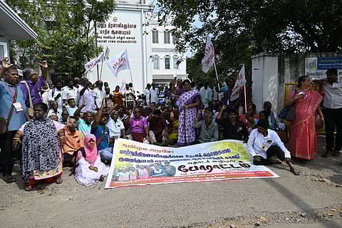 Many persons with disabilities gathered together raising their arms, holding flags, and chanting with a large banner in front.
