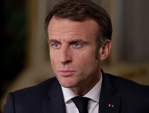 Image of French President Emmanuel Macron in a black suit and black tie. The background is blurred.