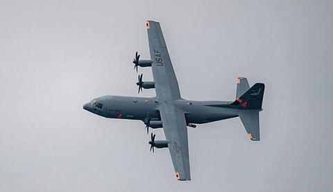 USAF military transport aircraft in flight, viewed from below. The gray plane, with four propellers, flies against a cloudy sky, suggesting motion and strength.