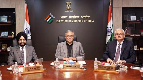CEC Gyanesh Kumar and ECs Dr. Sukhbir Singh Sandhu and Dr. Vivek Joshi sitting at a table in the ECI building, smiling at the camera.