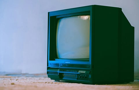A vintage black CRT television sits on a dusty floor, tilted slightly to the left. The setting suggests nostalgia and evokes a retro vibe.