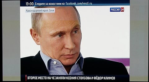 Image of Vladimir Putin on TV. Rostov-on-Don, Russia. He is in a suit and blue shirt looks serious while appearing on a news channel broadcast. The screen displays Russian text and a website link.