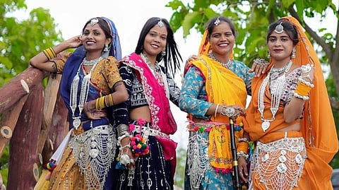 Four women pose dressed in saaris and silver, smiling at the camera.