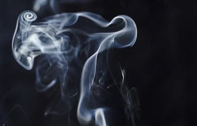 Wispy white smoke curls gracefully against a dark background, creating a mysterious and ethereal atmosphere with its flowing and delicate patterns.