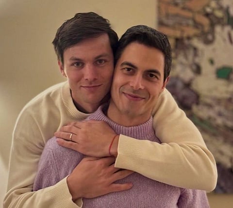 Image of  Netherlands’ First Gay Prime Minister, Rob Jetten and his fiance Nicolás Keenan smiling warmly, embracing in cozy sweaters. The atmosphere is intimate and cheerful, with a blurred background adding depth to the scene.
