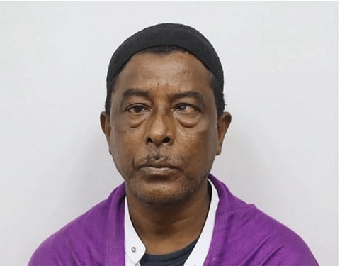 A close up of Nurul Amin Shah Alam, wearing a cap and a purple sweater.