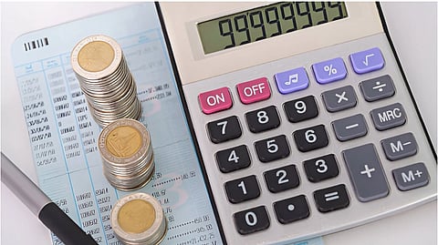 Stacks of coins on a financial statement beside a calculator displaying 9,999,945. A pen lies nearby. The tone suggests financial analysis.