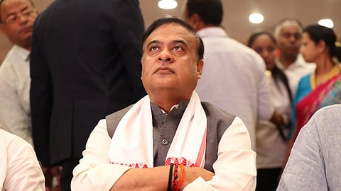 Himanta Biswa Sarma sits with arms crossed, looking up at a screen.