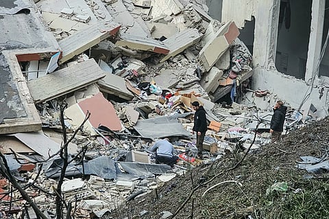 Two men stand by the rubble of a building