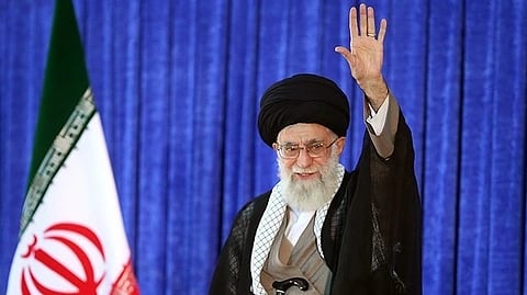 In the image Khamenei is shown weaving his hand behind him is blue screen and Iran flag