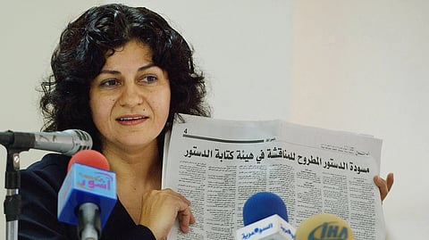 Yanar Mohammed sitting in front of mics, holding up a newspaper in arabic