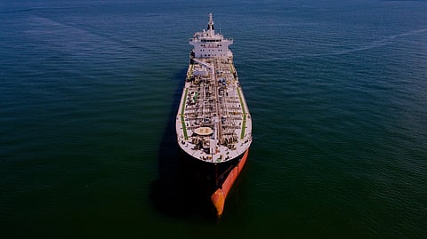 Aerial view of a large cargo ship at sea during sunset. The sky is vibrant with orange and pink hues, reflecting a calm and serene atmosphere.