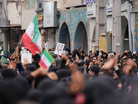 A funeral procession with people holding up Iranian flags and photos of children killed by US strikes.