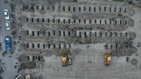 Aerial view of multiple rows of graves, with bulldozers digging more.
