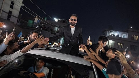 Balen Shah standing out of a sunroof while a crowd reaches out at him