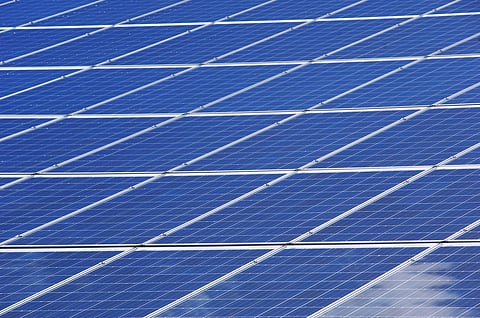 Close-up of blue solar panels arranged in rows, capturing sunlight on a clear day. The image conveys sustainability and renewable energy themes.