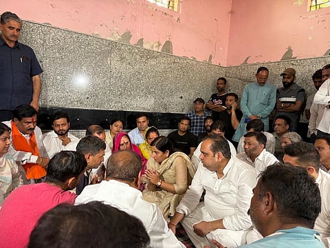Multiple people sitting on the ground, including BJP ministers and the victim's family