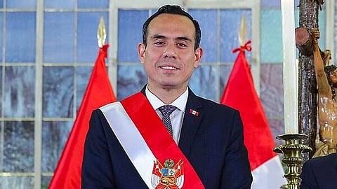 José Jerí standing in formals and a ceremonial sash in front of Peru's flag.