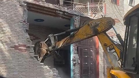 A bulldozer pulls down a brick wall of a house