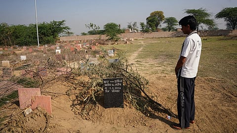 A man stands in front of the grave of 28-year-old Aamir Khan, which is covered in branches
