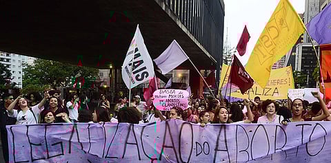 protestors hold up a banner and flags saying 'legalize abortion' in Spanish