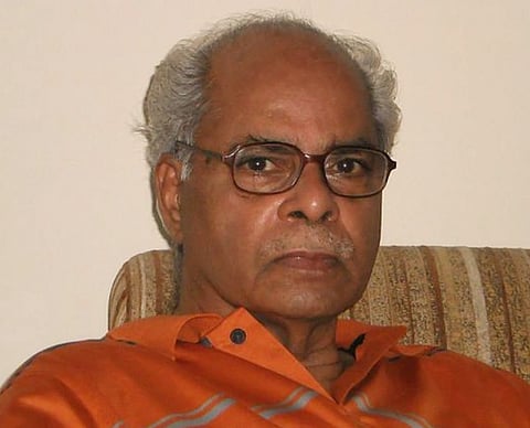Image of Indian historian K. N. Panikkar. the image is set in dim light. Panikkar is wearing glasses and is seated in a chair. 