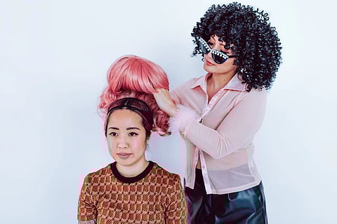 A woman in curly hair wearing goggles applying a pink frontal lace wig to another woman