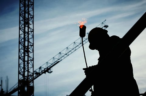 Silhouette of a construction worker with a blowtorch against a backdrop of cranes and a cloudy sky, conveying industrial themes and focus.
