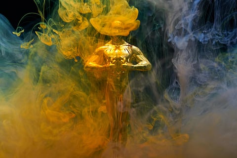 A golden figurine partially obscured by swirling clouds of vibrant yellow, blue, and gray smoke, creating a mysterious and ethereal atmosphere.