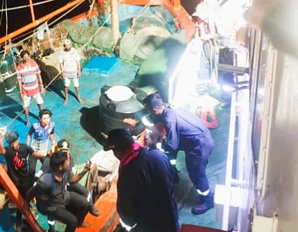 People are gathered on a boat at night, some seated and others standing. A crew member in uniform attends to tasks, creating a busy, urgent atmosphere.
