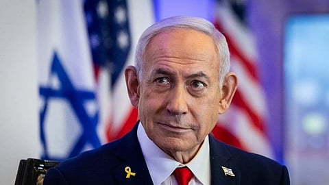 Benjamin Netanyahu in a suit with flags of Israel and USA blurred behind him, looking thoughtful. Blue ambient lighting sets a formal tone.