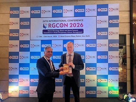 An event: 24th International conference: Rajiv Gandhi Cancer Institute and Research Centre, 2 men in suits, one presenting a book to another