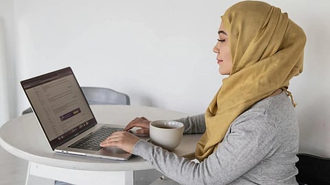 Muslim businesswoman typing on laptop during coffee break at home