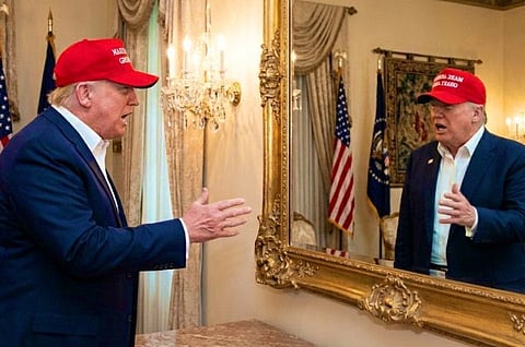 Image of President Donald Trump wearing a MAGA red cap and talking to himself in front of a huge mirror with a golden frame. 