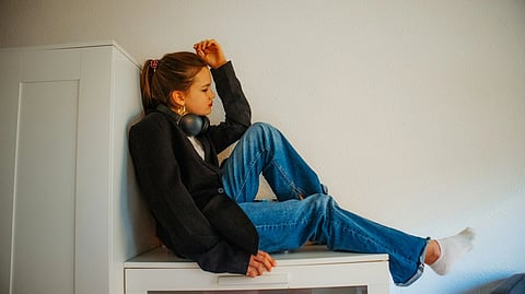 A teenage girls with headhnes sits sadly against a white background