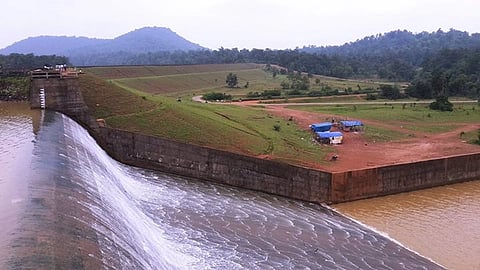 Water flows down a cement incline with fields, red sand and mountains in the background