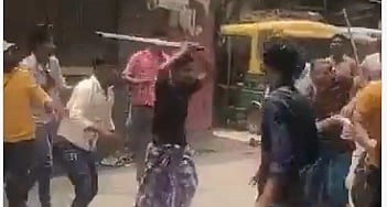 A group of men in a street altercation; one raises a stick aggressively, others appear defensive. An auto-rickshaw is parked in the background. Tense scene before West bengal election 2026
