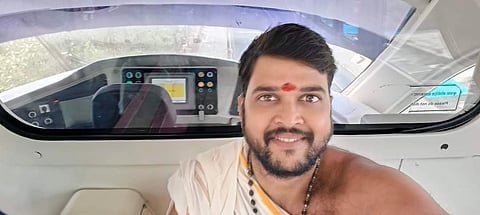 Hrishikesh Vaidya in traditional attire with a red mark on his forehead smiles inside a modern vehicle cockpit