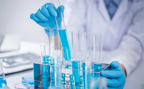 A scientist in a white lab coat and blue gloves carefully handles test tubes filled with blue liquid, conveying precision and focus in a laboratory setting.