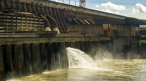 Massive concrete dam releasing water with force, generating mist. Clear blue sky and fluffy clouds enhance the majesty of the structure.