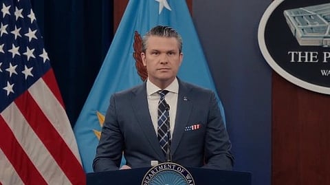 In the image Pete Hegseth is shown adressing people behind him are america flags