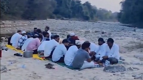 A group of men sit crosslegged on a met at a rivershore