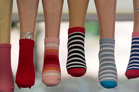 Display of mannequins wearing varied ankle socks: solid red, pink with stripes, black and white striped, and blue with white stripes, against a blurred background.