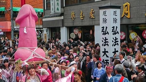 In the image a large pink Phallus is shown with people carrying it