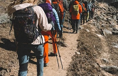 A group of hikers with backpacks and trekking poles walk in a single file along a rocky mountain trail, conveying a sense of adventure and camaraderie.