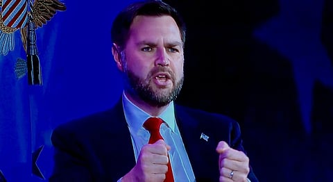 Image of JD Vance at the MAHA Summit in DC. his hands are folded and are gesturing something. the image has ablueish tint to it. 