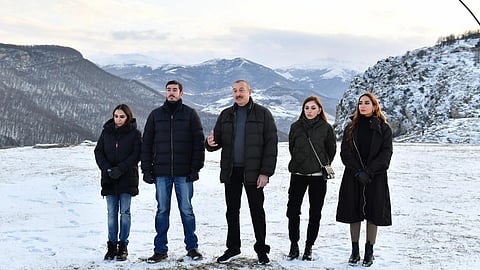 A group of five people stands together on a snowy landscape with mountains in the background. They are dressed warmly in winter clothing, conveying a serene yet chilly atmosphere.
