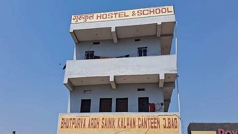 Three-story building with a sign reading "HOSTEL & SCHOOL" on top. Below, a canteen sign, "BHUTPURVA ARDH SAINIK KALYAN," against a clear blue sky.