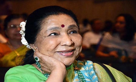 In the image Asha Bhosle is shown in a traditional attire in a formal gathering