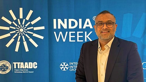 In the image Vinesh Chandel is shown smiling at the camera behind him is a backdrop where INDIA WEEK is written 
